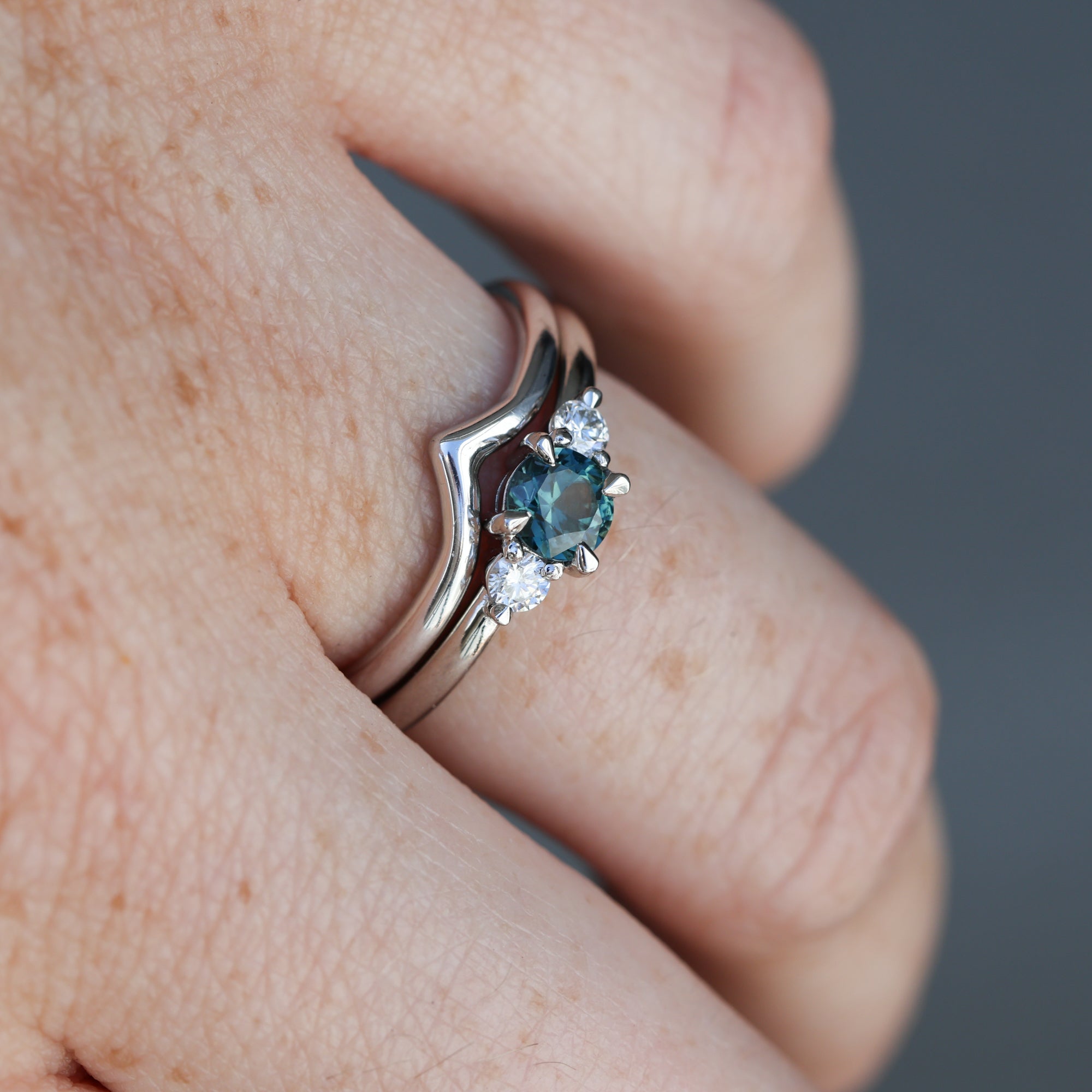 0.46ct round cut australian parti sapphire trilogy engagement ring on hand with wedding band