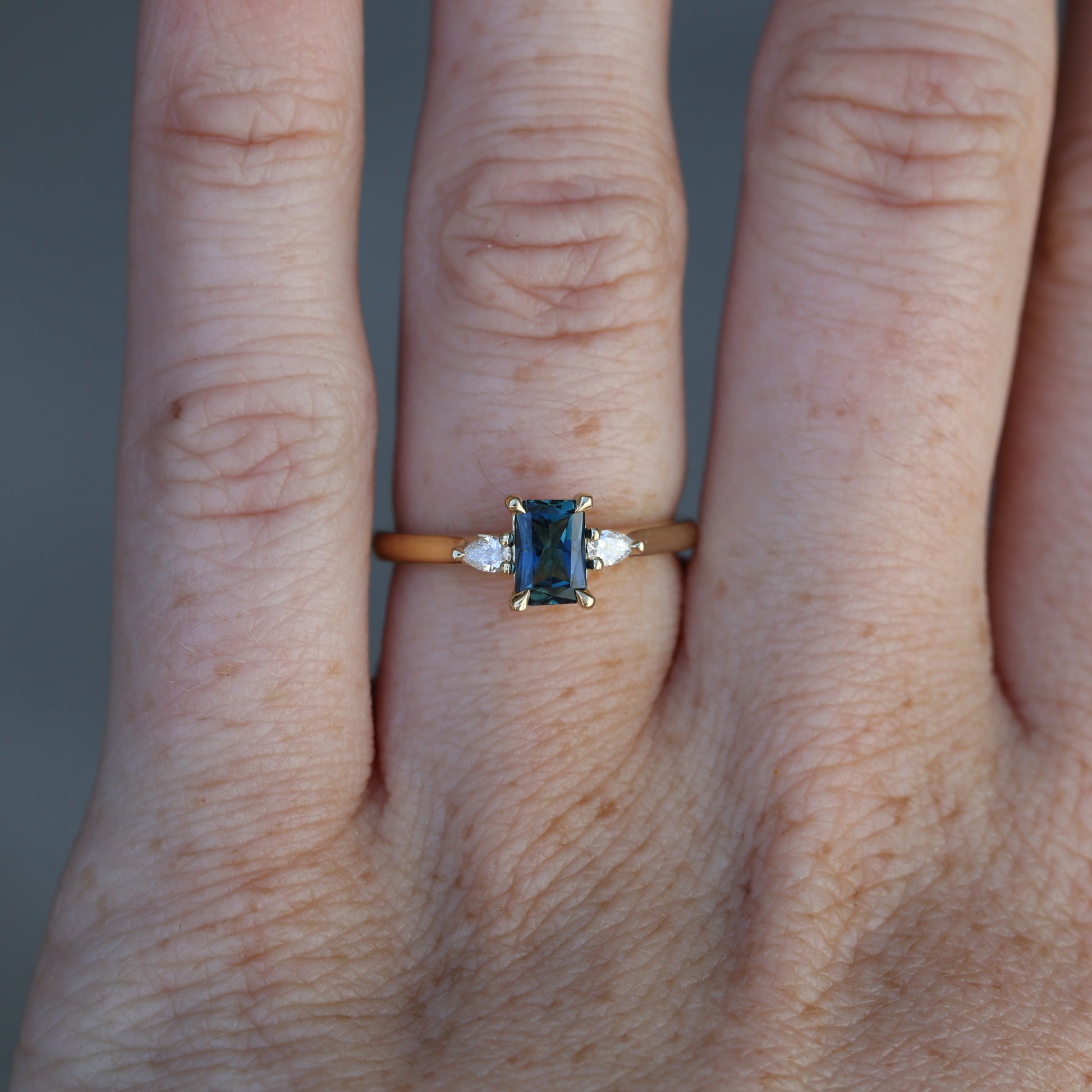 0.66ct Emerald cut australian sapphire trilogy engagement ring on hand