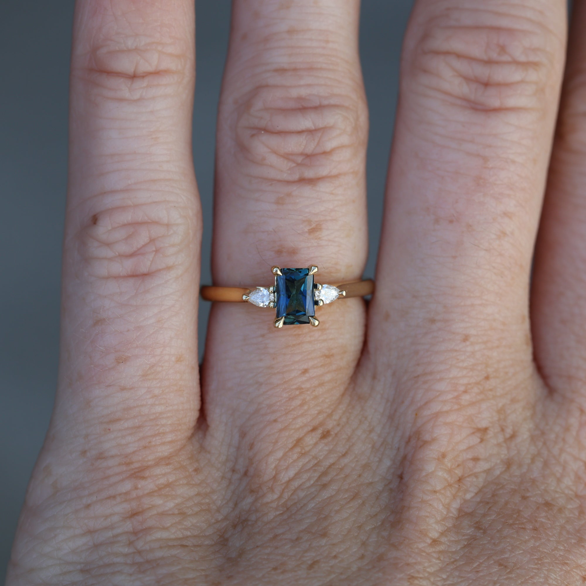 0.66ct Emerald cut australian sapphire trilogy engagement ring on hand