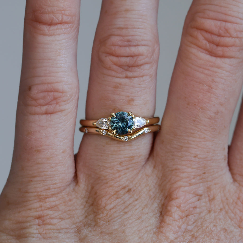 0.67ct Montana Sapphire and diamond May trilogy engagement ring on hand with wedding band