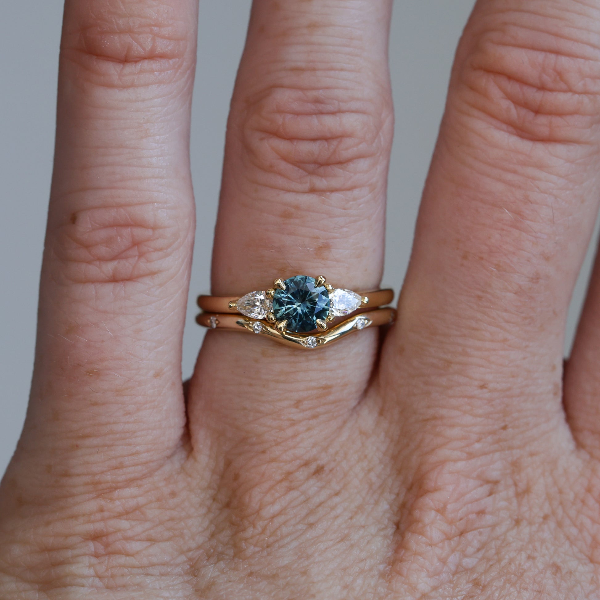 0.67ct Montana Sapphire and diamond May trilogy engagement ring on hand with wedding band