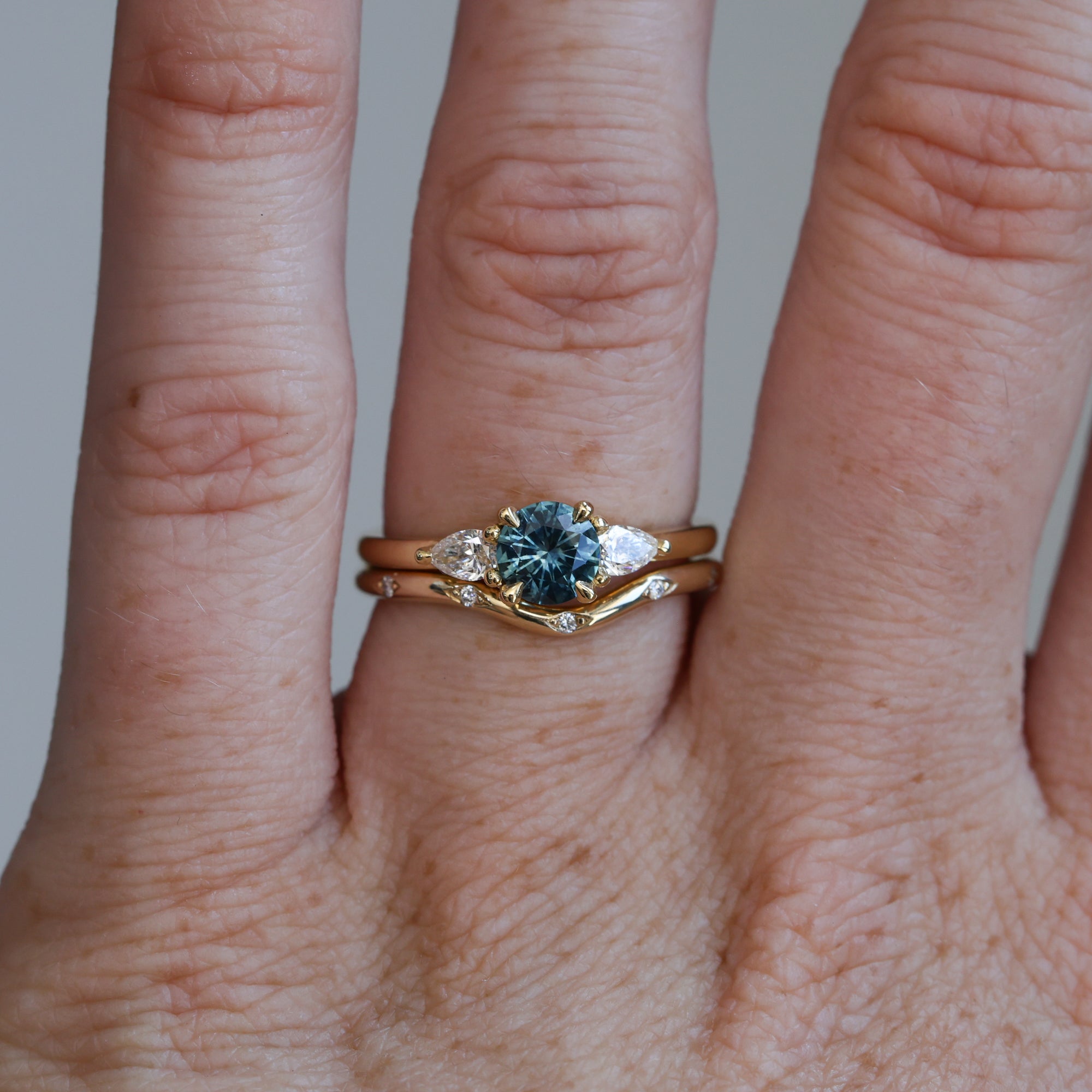 0.67ct Montana Sapphire and diamond May trilogy engagement ring on hand with wedding band