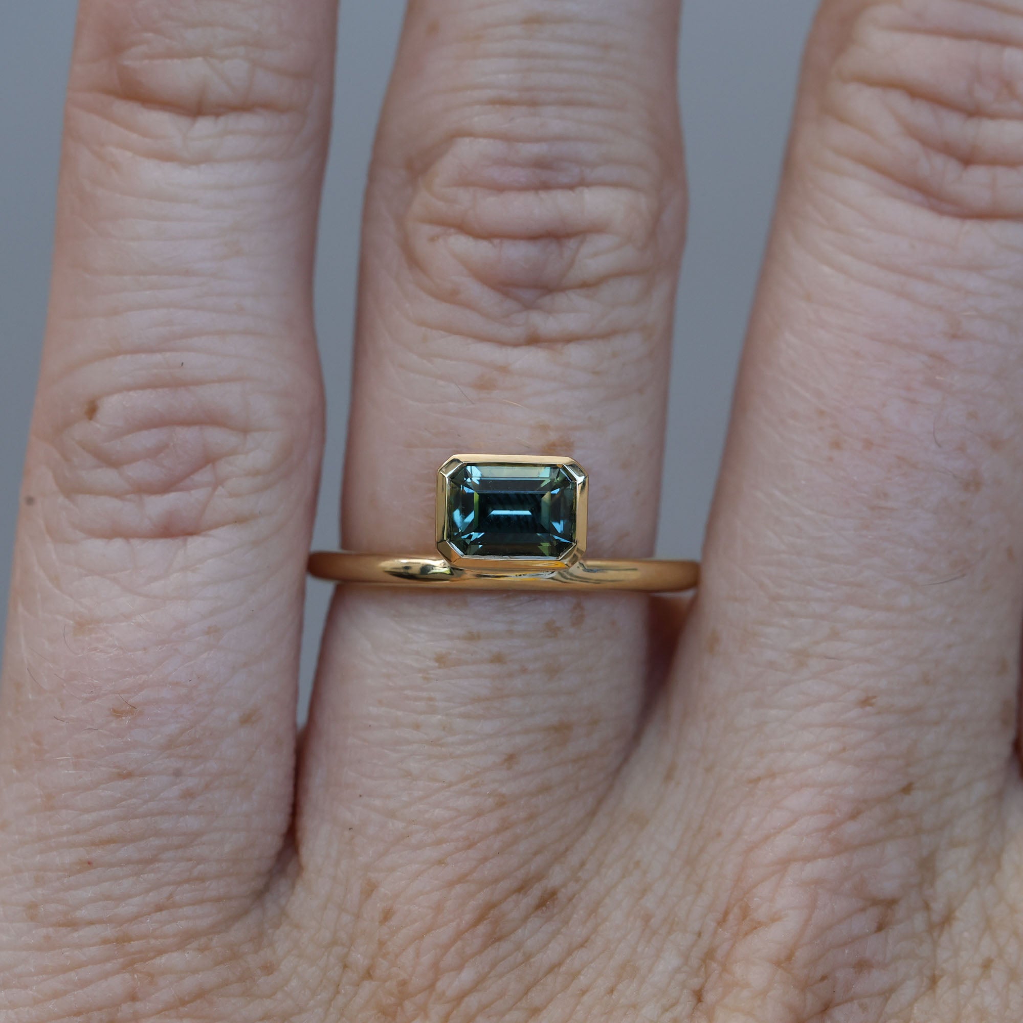 0.84ct emerald cut australian parti sapphire offset bezel engagement ring on hand