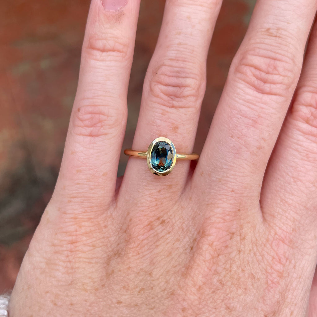 Bezel set oval cut Australian parti sapphire engagement ring in 18ct yellow gold  on hand