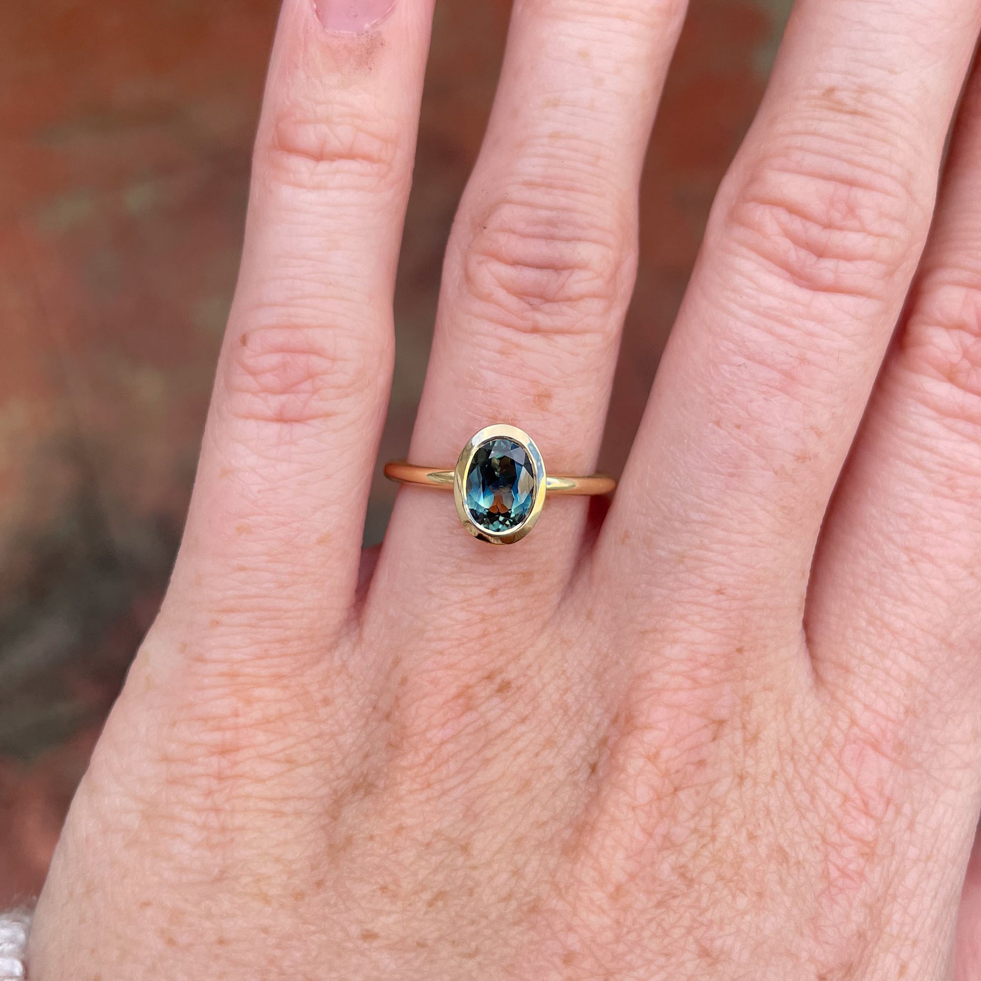 Bezel set oval cut Australian parti sapphire engagement ring in 18ct yellow gold  on hand