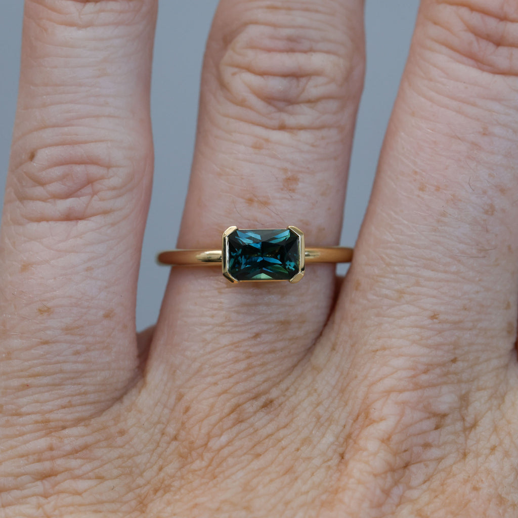 1.20ct emerald cut australian parti saphire east west semi bezel engagement ring on hand