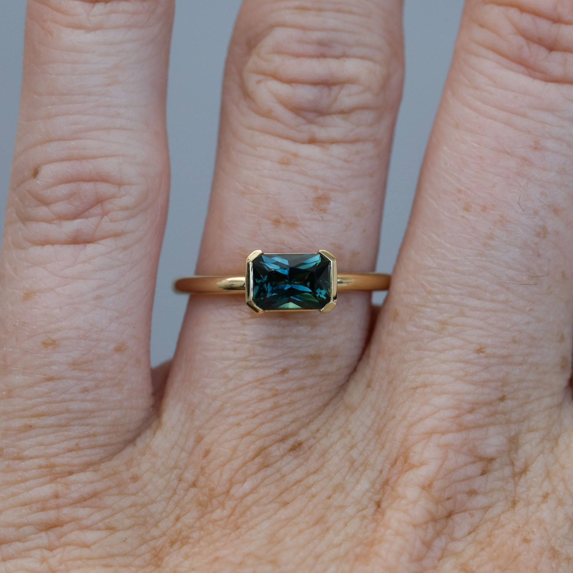 1.20ct emerald cut australian parti saphire east west semi bezel engagement ring on hand