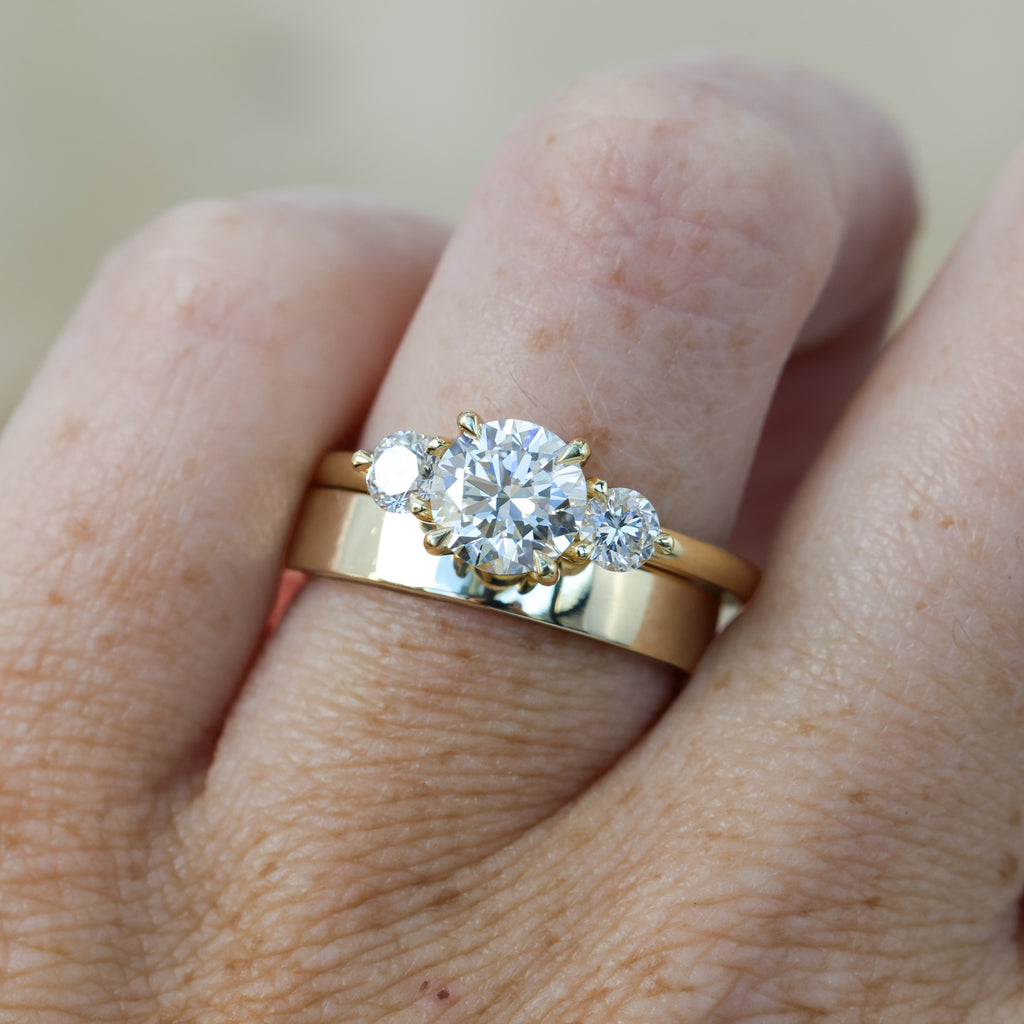 diamond round cut trilogy engagement ring yellow gold on hand with wedding band
