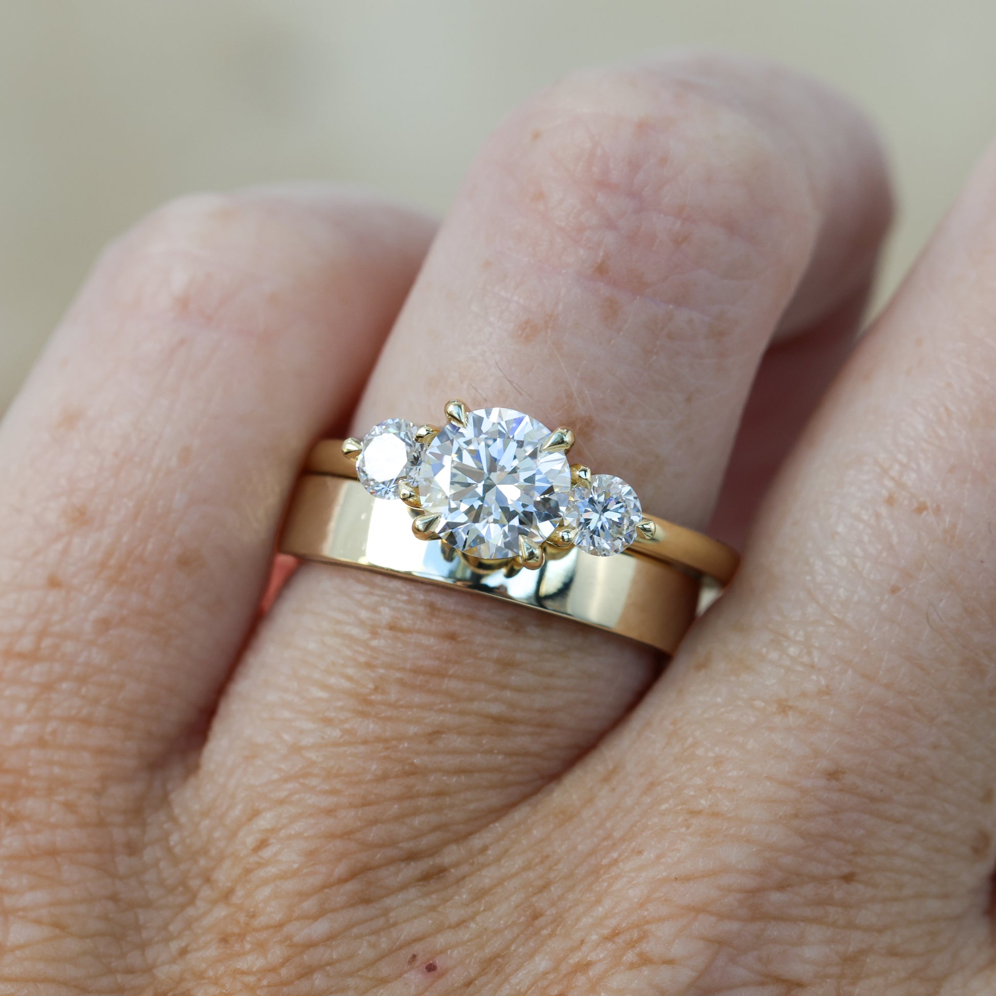 diamond round cut trilogy engagement ring yellow gold on hand with wedding band