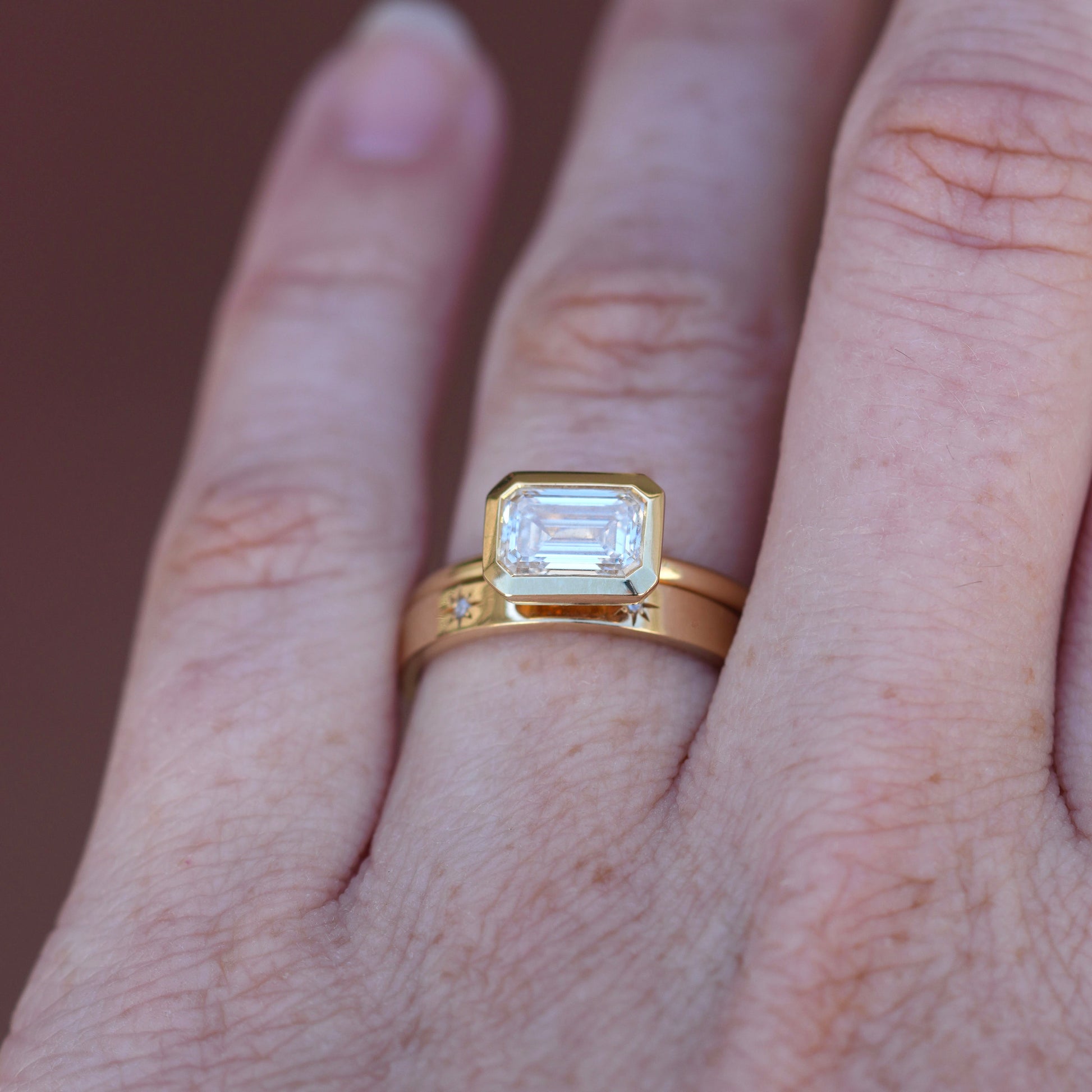 1.36ct Emerald Cut Bezel Engagement ring on hand with wedding band
