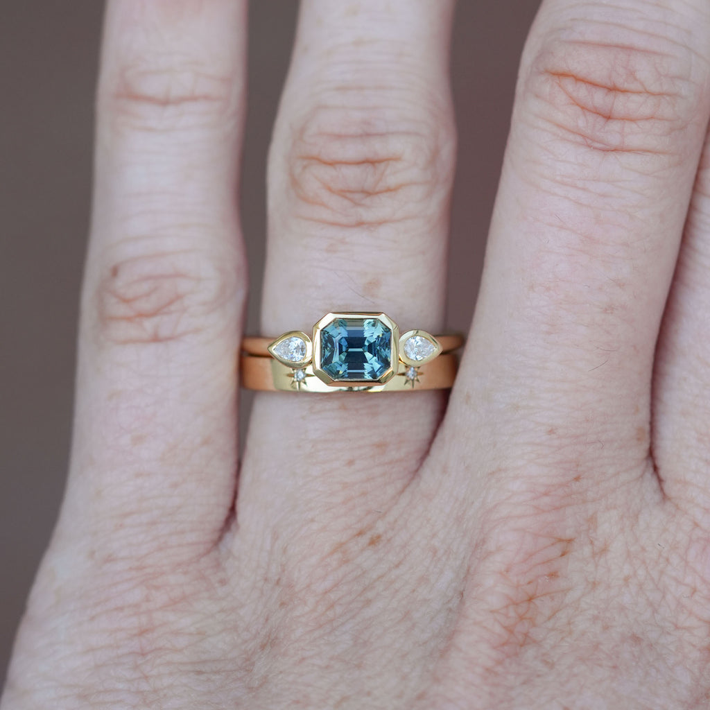 1.51ct Madagascan Sapphire Bezel trilogy engagement ring on hand with wedding band